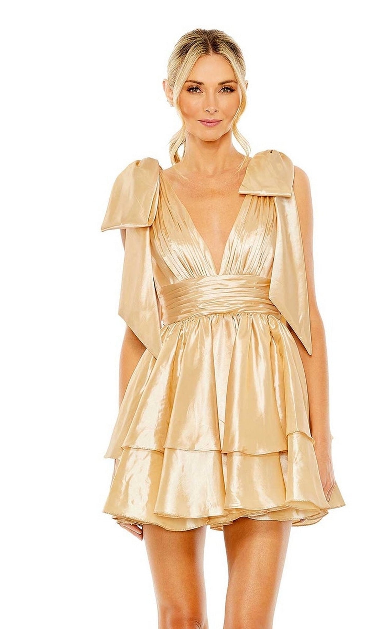 A woman models the Mac Duggal 11657 Bow Short Ruffled Hoco Dress—a shiny gold, sleeveless mini with tiered ruffles, a deep V-neckline, and large shoulder bows—against a white background.